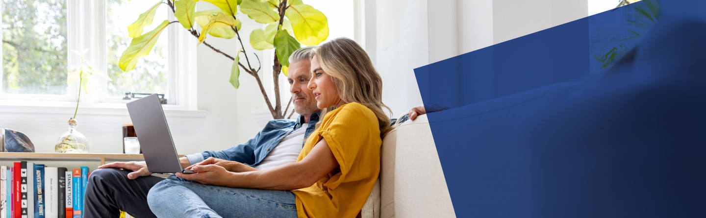 Headerbild Eine Frau und ein Mann sitzen nebeneinander entspannt auf dem Sofa mit einem Laptop auf dem Schoß 