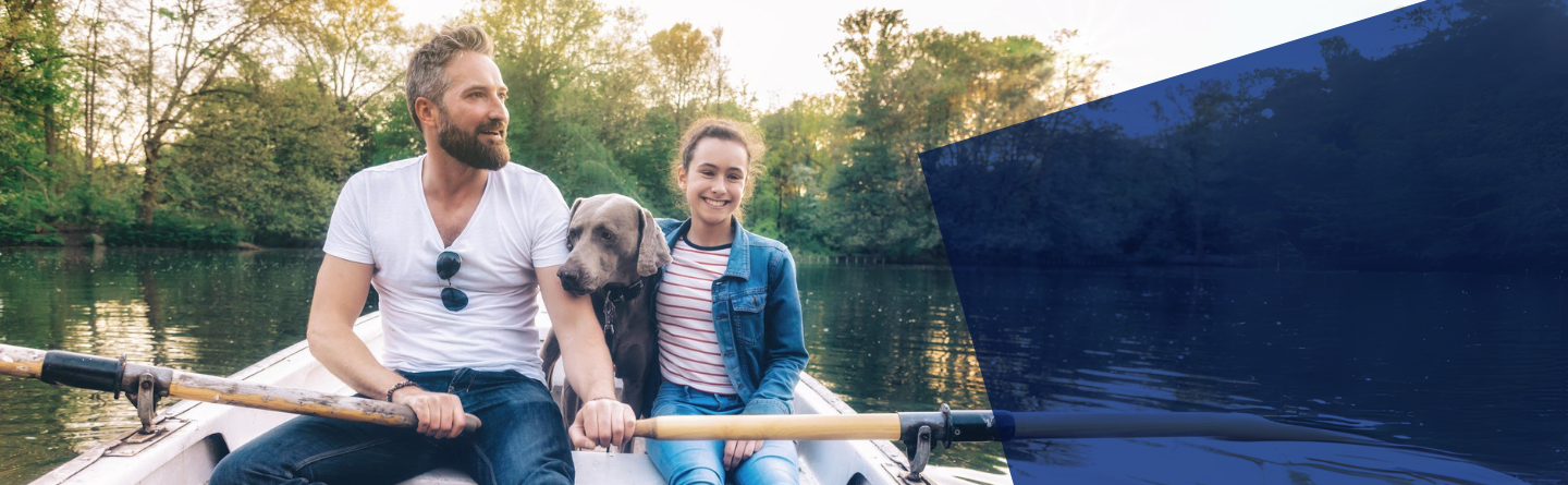 Header Vater, Tochter und Hund sitzen in einem kleinen Ruderboot auf einem See umrundet von Bäumen