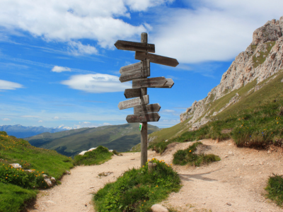 Bergige Landschaft mit verschiedenen wegen und einem Wegweiser aus Holz in verschiedene Richtungen